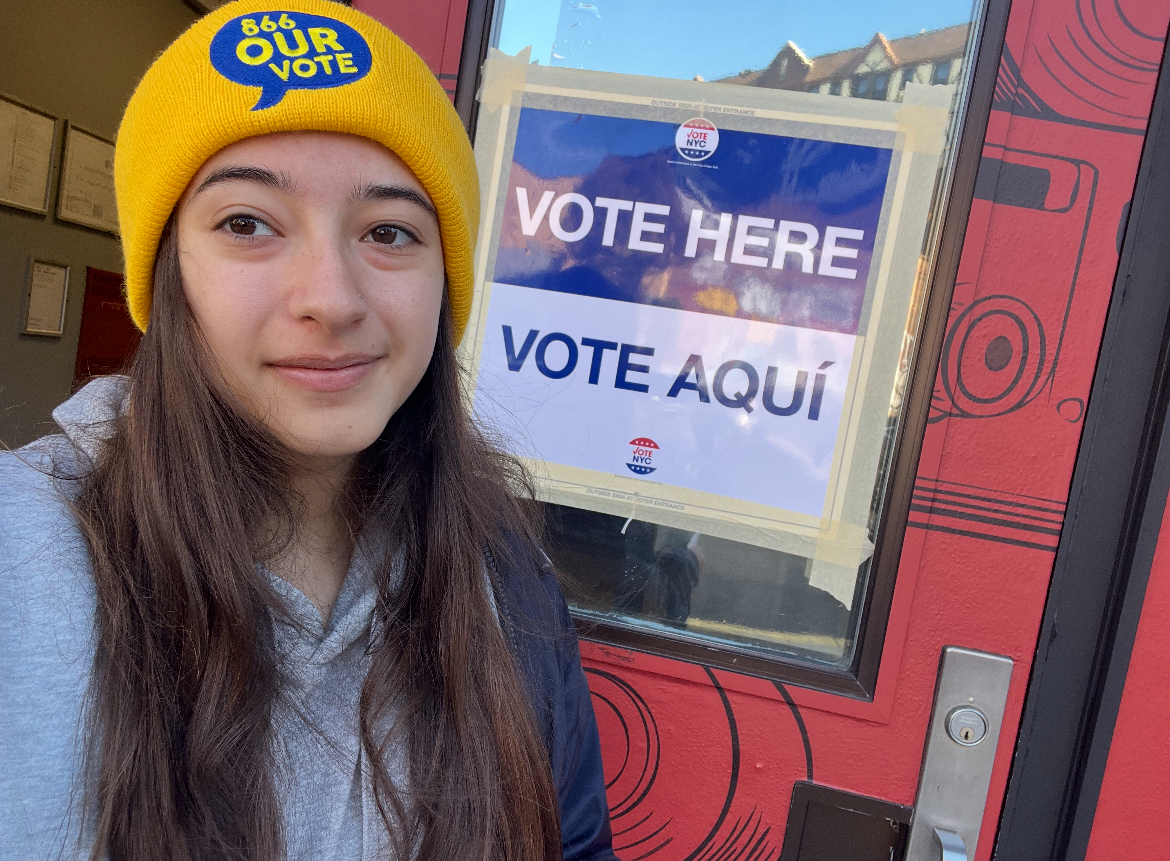 Young volunteer beside a multilingual polling place sign